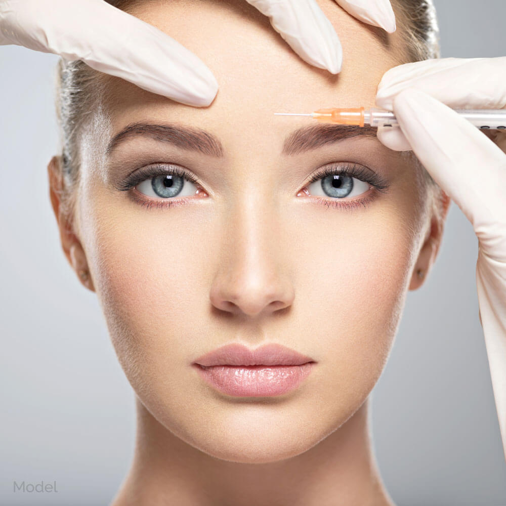 Female model receiving an injection in her forehead from a doctor's hands