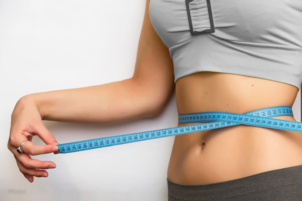 Mid-body shot of a woman wrapping measuring tape around her midriff