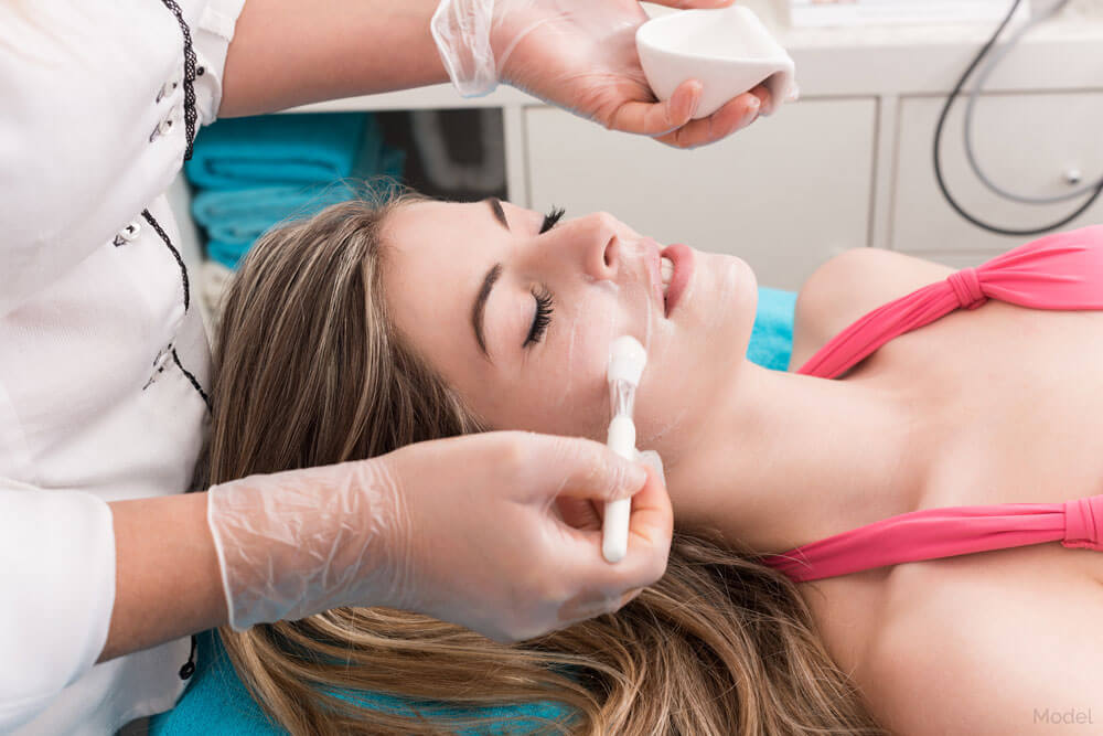 Young woman laying on surgical bed receiving non-surgical treatment from a doctor on her face