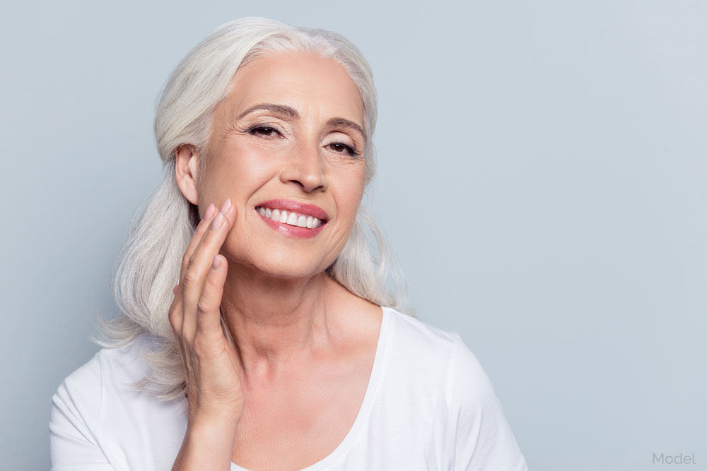 Middle aged woman smiling while rubbing her smooth facial skin