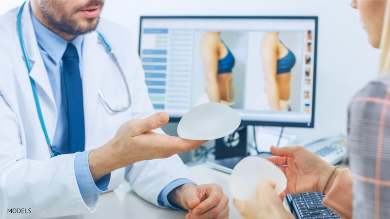 Plastic surgeon reviewing breast implant options with patient during consultation.