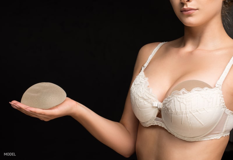 Woman holding a breast implant in her hand against a black background.